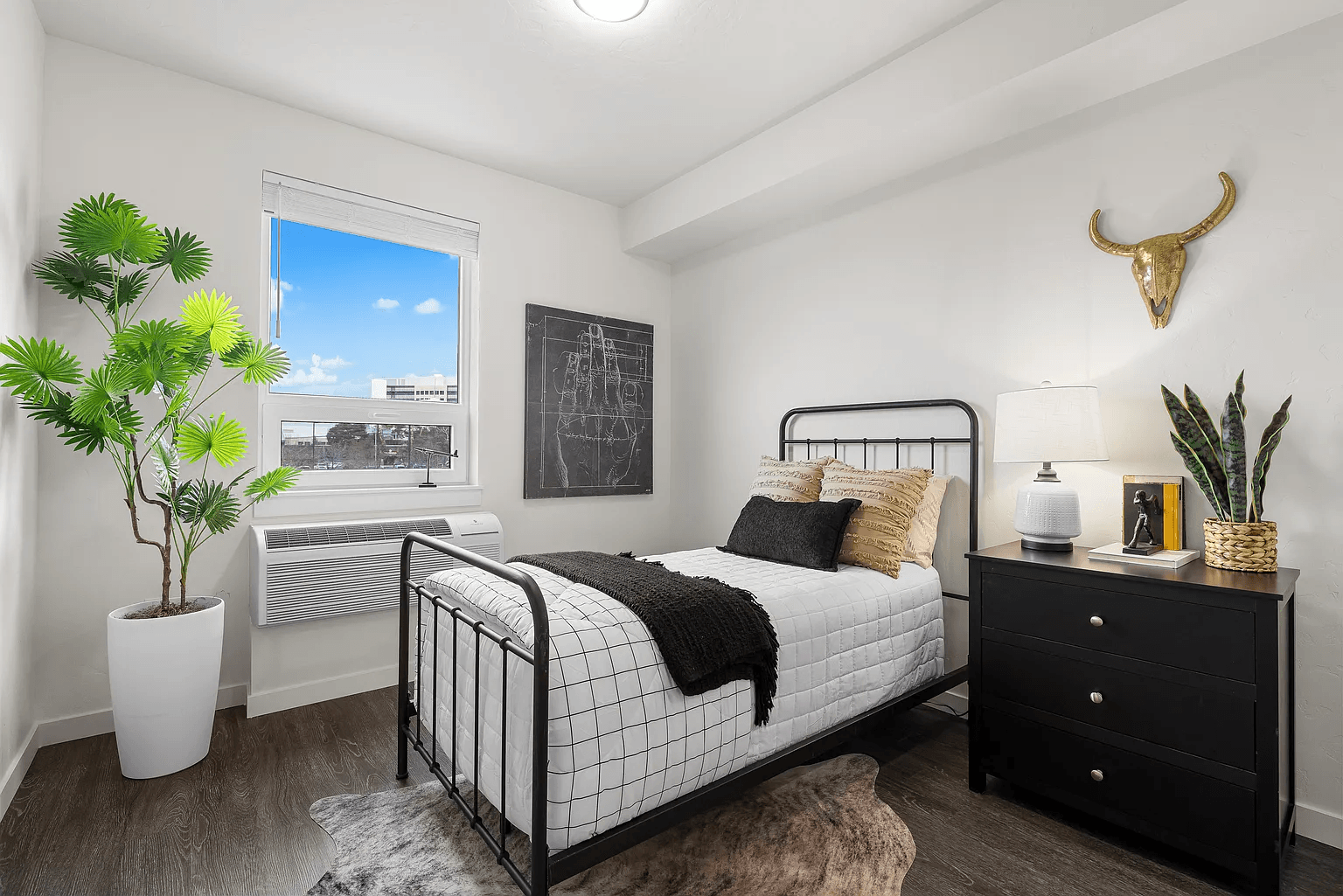 A bedroom with a black and white bed, a black dresser, and a plant in a white pot.